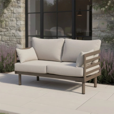 Beige outdoor sofa with metal frame and cushions on patio beside stone wall and glass doors