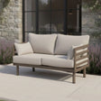 Beige outdoor sofa with metal frame and cushions on patio beside stone wall and glass doors