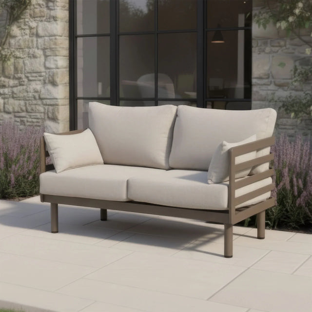 Beige outdoor sofa with metal frame and cushions on patio beside stone wall and glass doors