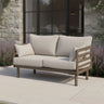 Beige outdoor sofa with metal frame and cushions on patio beside stone wall and glass doors