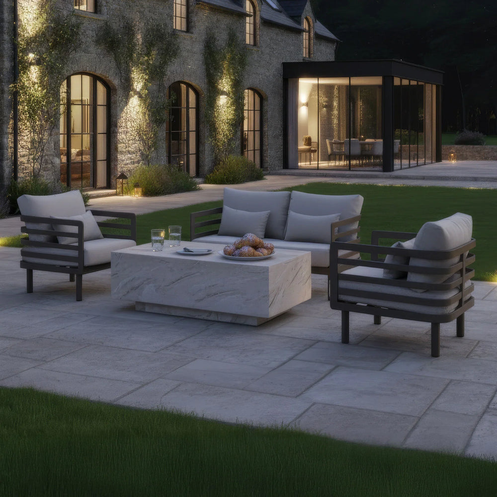 Outdoor garden furniture set with cushioned chairs and marble table on stone patio at dusk
