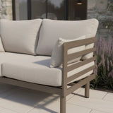 Light beige outdoor sofa with metal frame and cushions on patio beside garden flowers