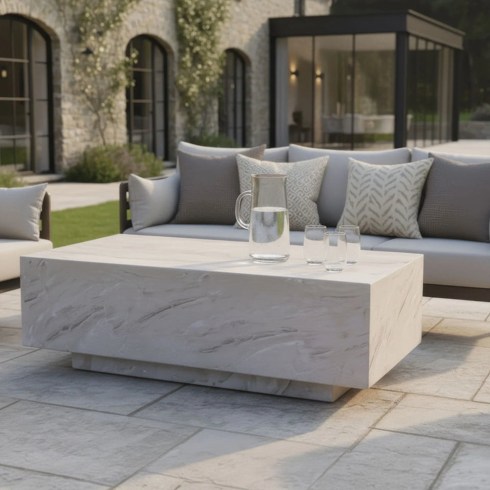 Rectangular stone outdoor coffee table with glass jug and tumblers on patio