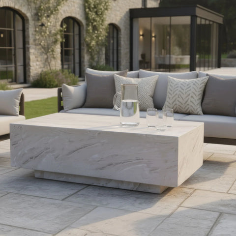 Rectangular stone outdoor coffee table with glass jug and tumblers on patio