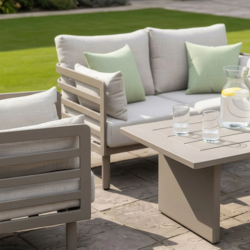 Beige outdoor sofa set with matching armchair, square table and green cushions on patio