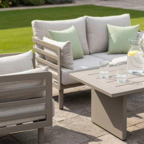 Beige outdoor sofa set with matching armchair, square table and green cushions on patio