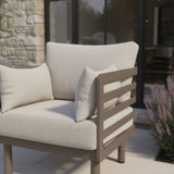 Beige outdoor armchair with thick cushions and metal slatted armrest on patio