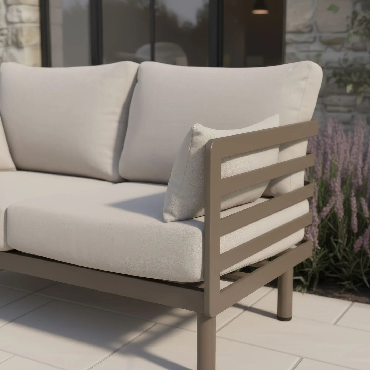 Outdoor sofa with beige cushions and taupe metal frame on patio next to garden lavender