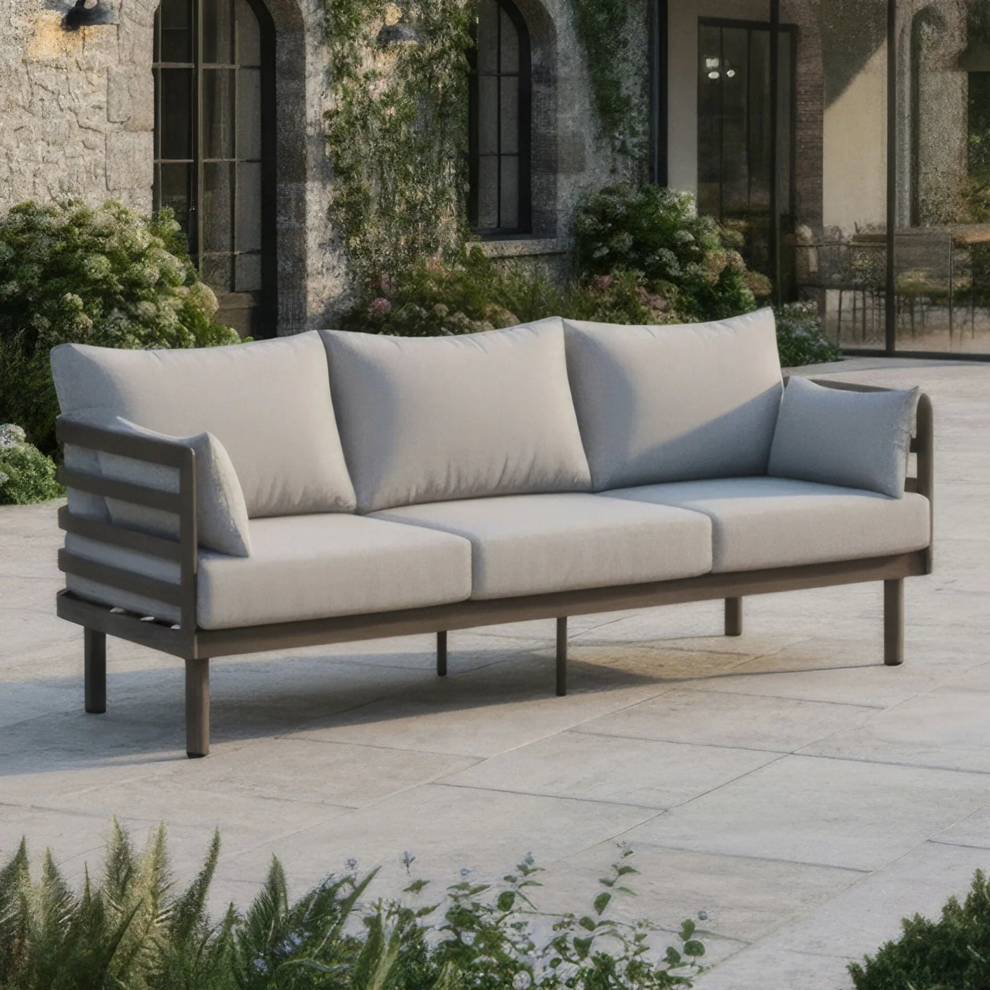 Grey outdoor sofa with metal frame and cushions on stone patio in garden setting