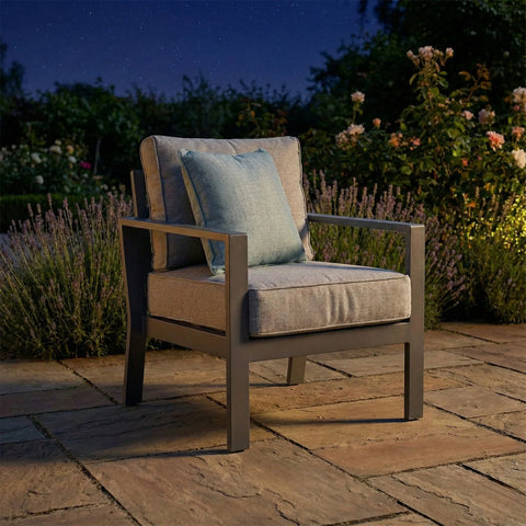 Outdoor patio chair with grey metal frame, beige cushions, and blue accent pillow at night