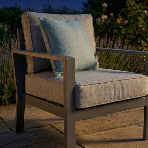 Grey outdoor armchair with metal frame and blue cushion on patio at dusk