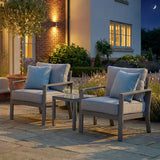 Grey outdoor garden armchairs with cushions and side table on stone patio at dusk