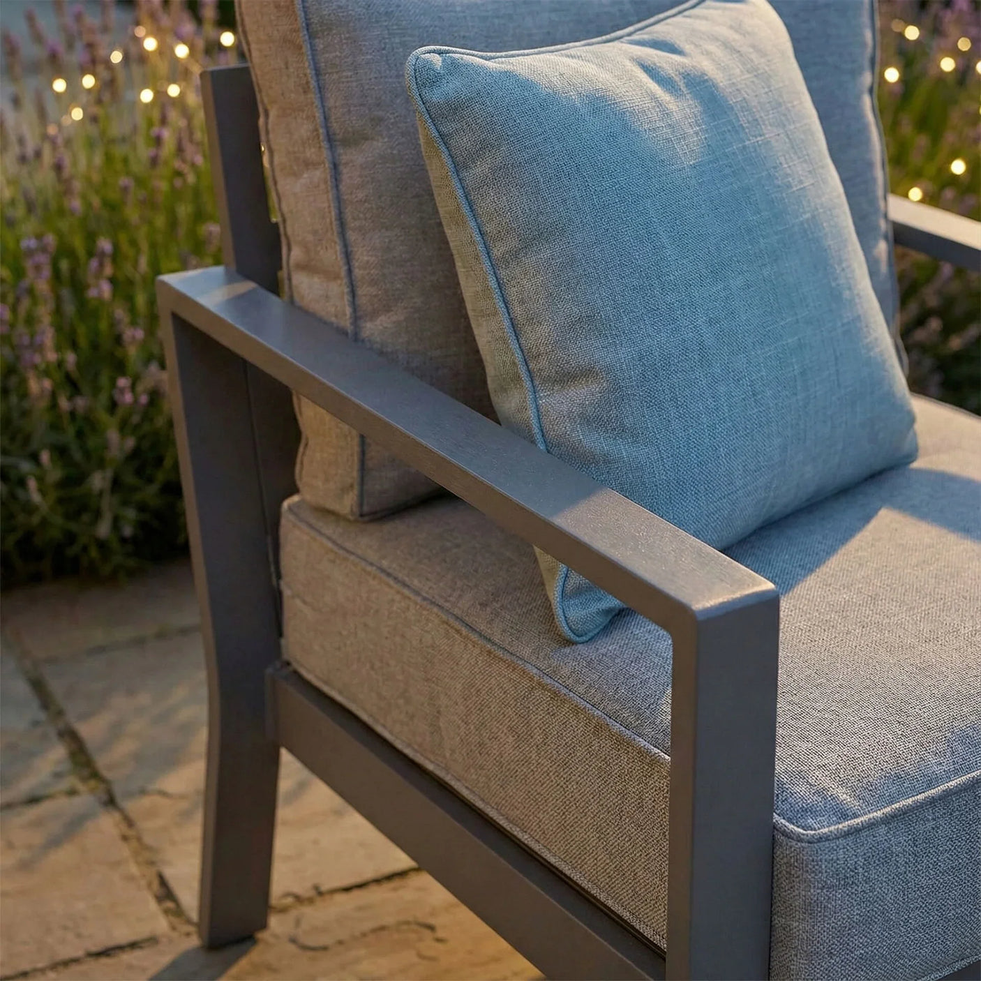 Grey outdoor armchair with metal frame and matching cushion on stone patio