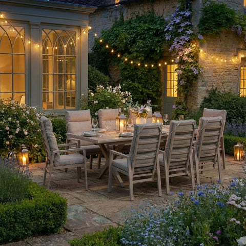 Wooden garden dining set with padded chairs on patio, lanterns and string lights at dusk