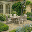Wooden outdoor dining set with six cushioned chairs on stone patio in country garden