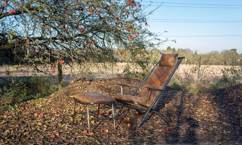 Brown leather recliner chair with matching footstool outdoors under apple tree
