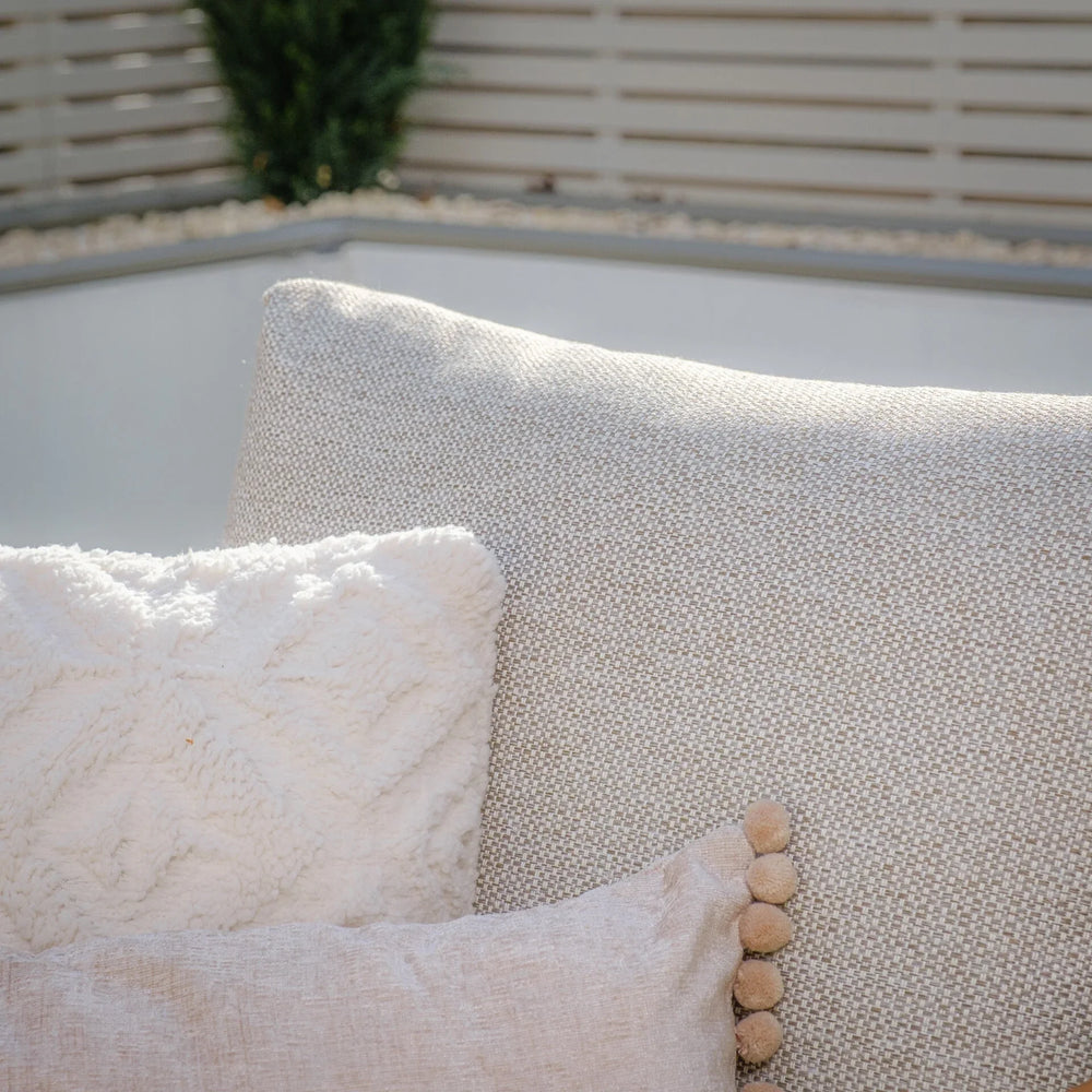 Close-up of beige sofa back with textured cream throw pillow and decorative cushion
