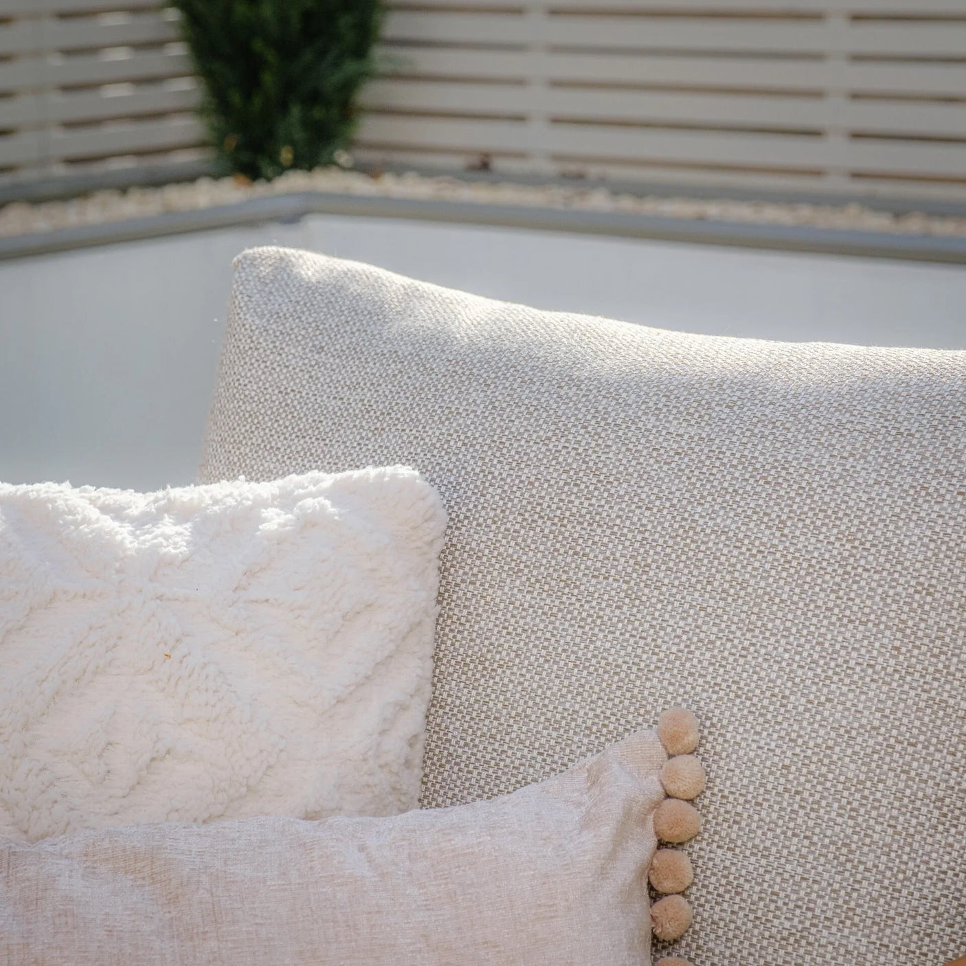 Close-up of beige sofa back with textured cream throw pillow and decorative cushion