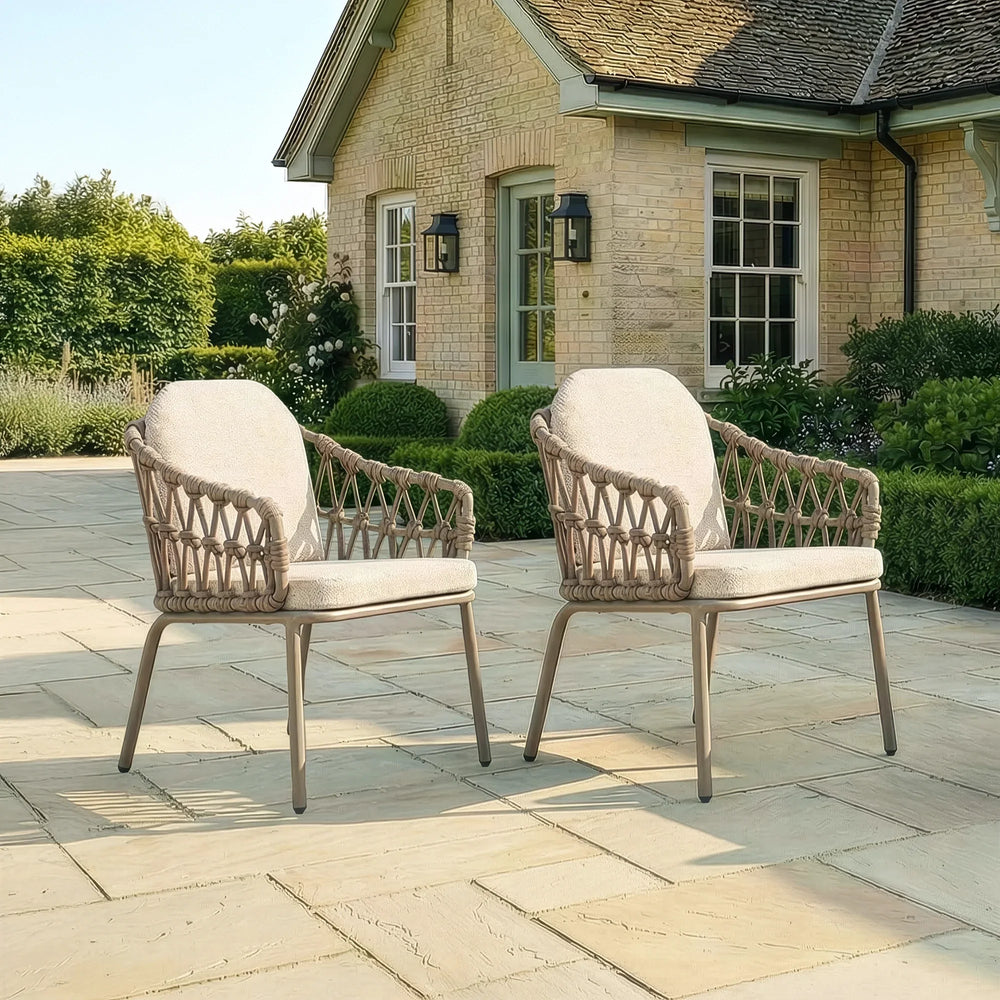 Pair of rattan outdoor garden chairs with cushions on stone patio in front of house