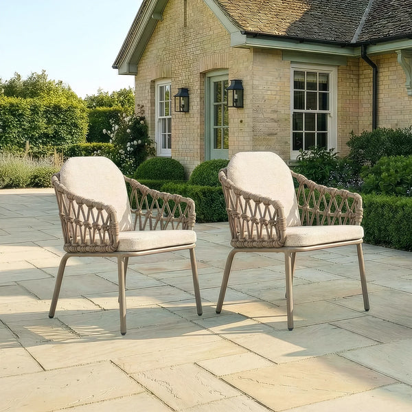 Pair of rattan outdoor garden chairs with cushions on stone patio in front of house