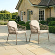 Pair of rattan outdoor garden chairs with cushions on stone patio in front of house