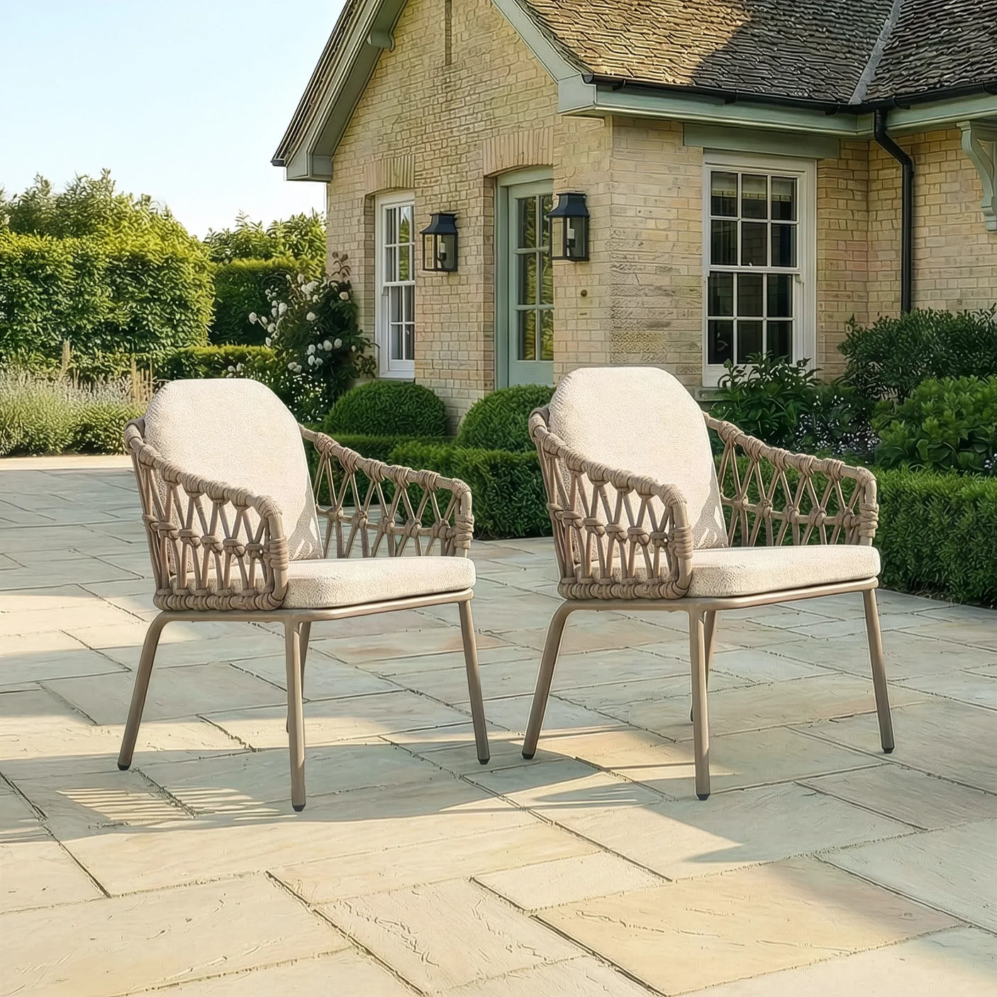 Pair of rattan outdoor garden chairs with cushions on stone patio in front of house