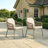 Pair of rattan outdoor garden chairs with cushions on stone patio in front of house