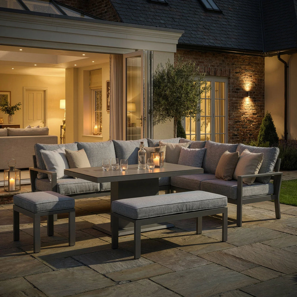 Grey outdoor garden sofa set with cushions, stools, and dining table on a patio at dusk