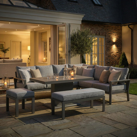 Grey outdoor garden sofa set with cushions, stools, and dining table on a patio at dusk