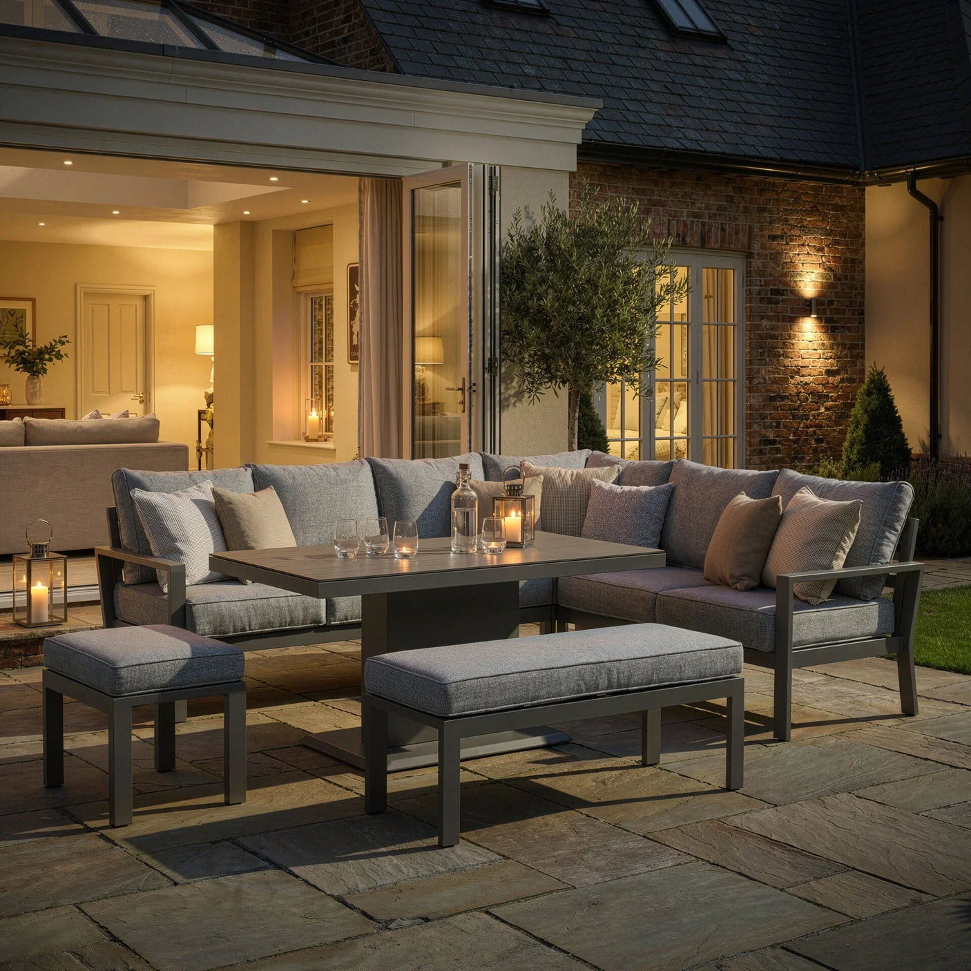 Grey outdoor garden sofa set with cushions, stools, and dining table on a patio at dusk