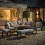 Grey outdoor garden sofa set with cushions, stools, and dining table on a patio at dusk