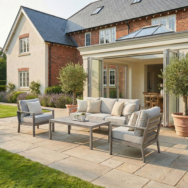 Grey outdoor sofa set with cushions and coffee table on stone patio in garden setting