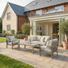 Grey outdoor sofa set with cushions and coffee table on stone patio in garden setting