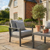 Grey outdoor garden lounge chair with cushions beside coffee table on paved patio