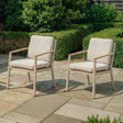 Outdoor armchairs with beige cushions and wooden arms on stone patio in garden setting