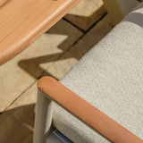 Close-up of outdoor dining chair with wooden armrest and beige cushion beside wooden table