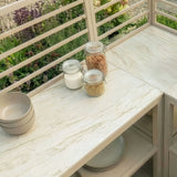 Outdoor kitchen worktop with beige stone surface, glass storage jars, and stacked bowls