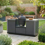 Outdoor kitchen with charcoal barbecue grill and cabinets on a patio in a landscaped garden