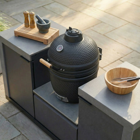 Black outdoor kamado grill in modern garden kitchen with prep counter and utensils