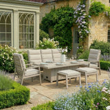 Beige cushioned outdoor dining set with table, chairs and benches on a stone patio in garden