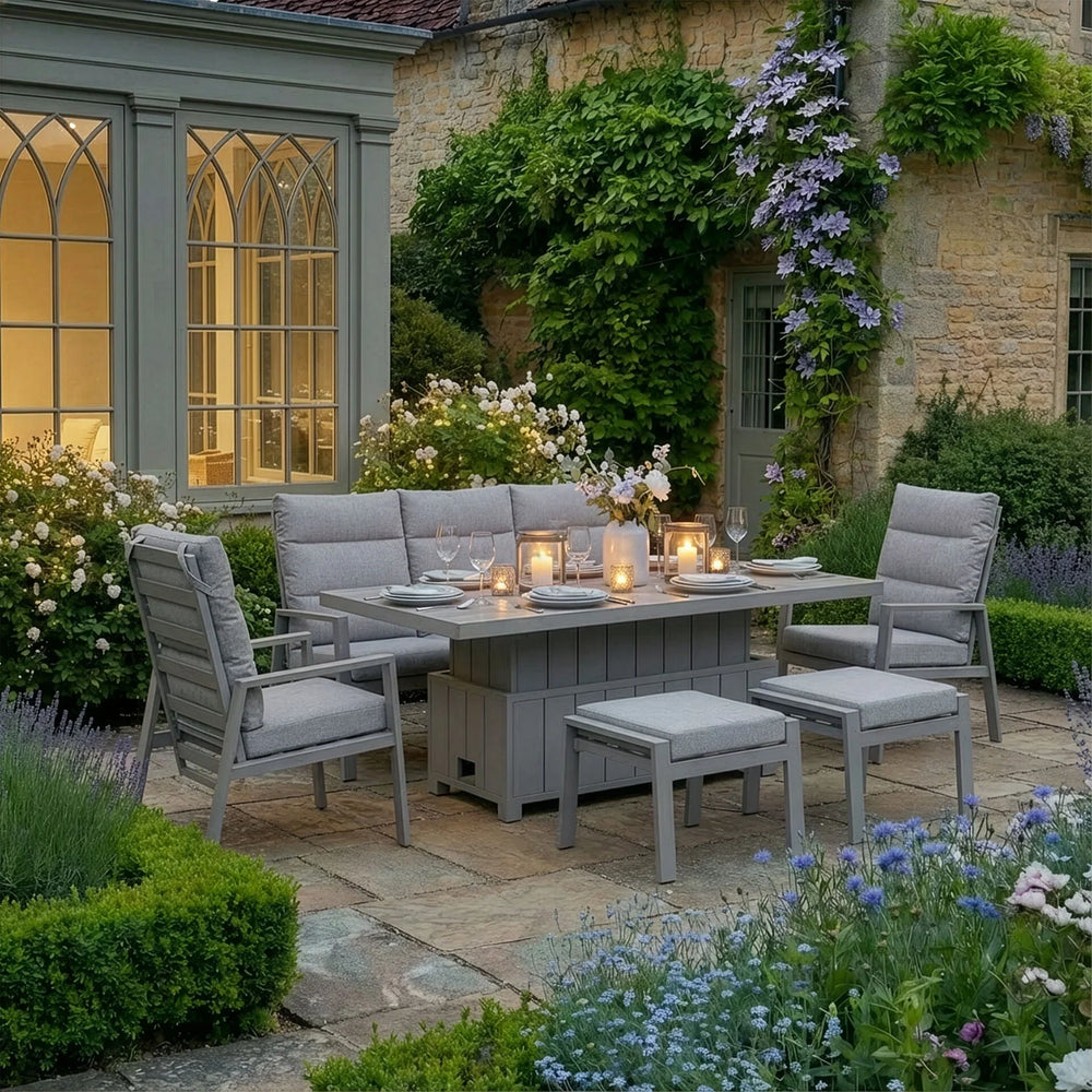 Grey outdoor dining set with cushioned chairs and benches on stone patio, set for evening meal