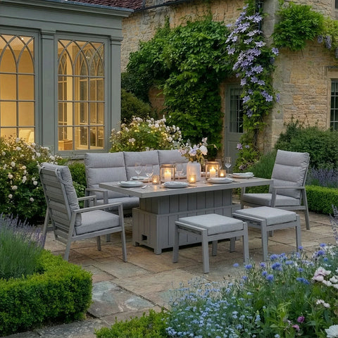 Grey outdoor dining set with cushioned chairs and benches on stone patio, set for evening meal