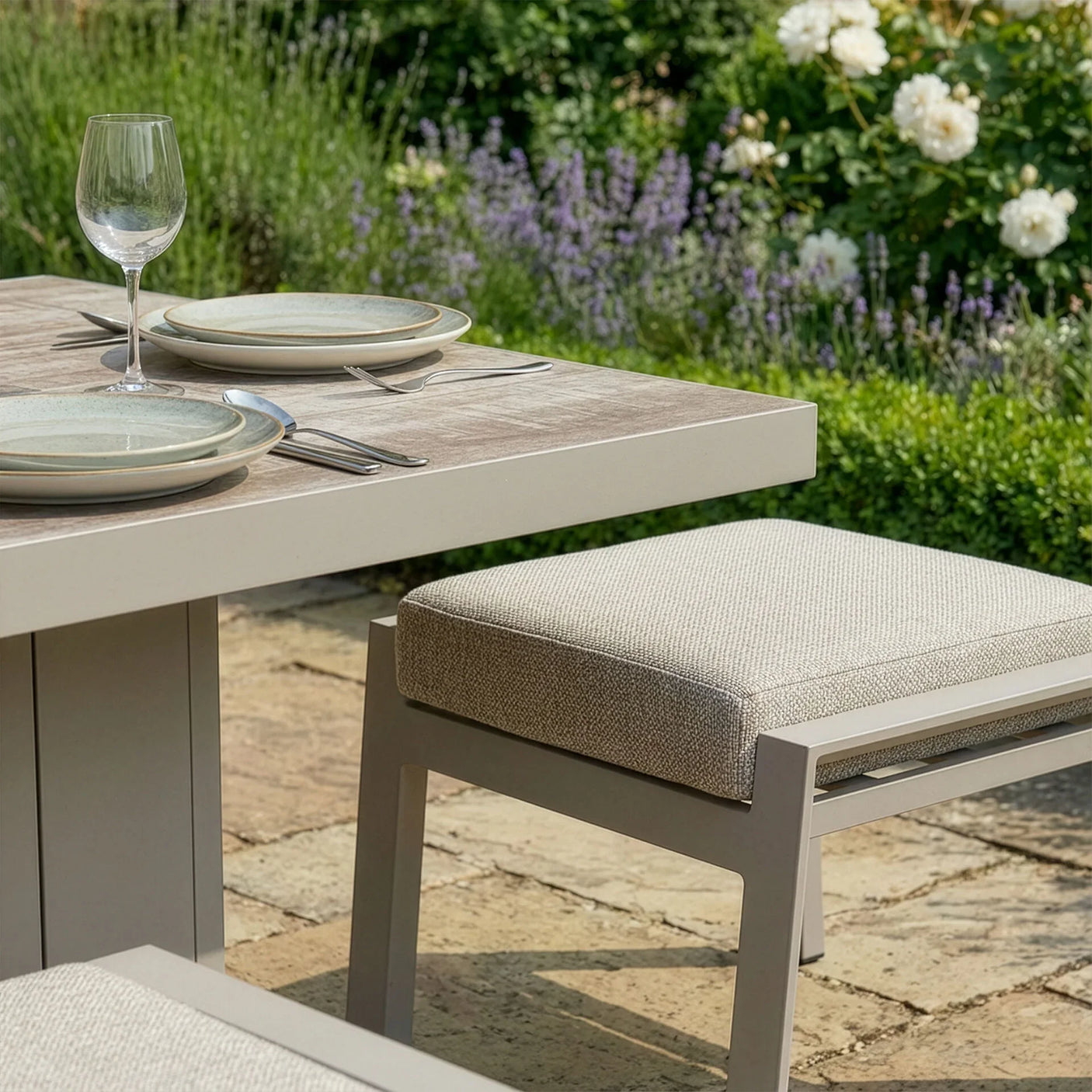 Modern garden dining table set with cushioned bench and plates on patio