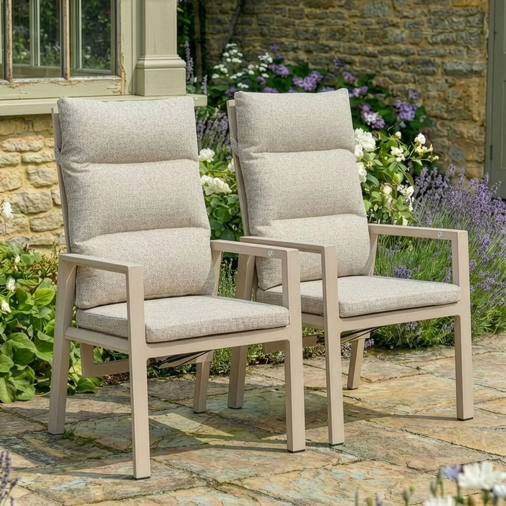 Beige cushioned garden dining chairs on stone patio with flowers and stone wall background