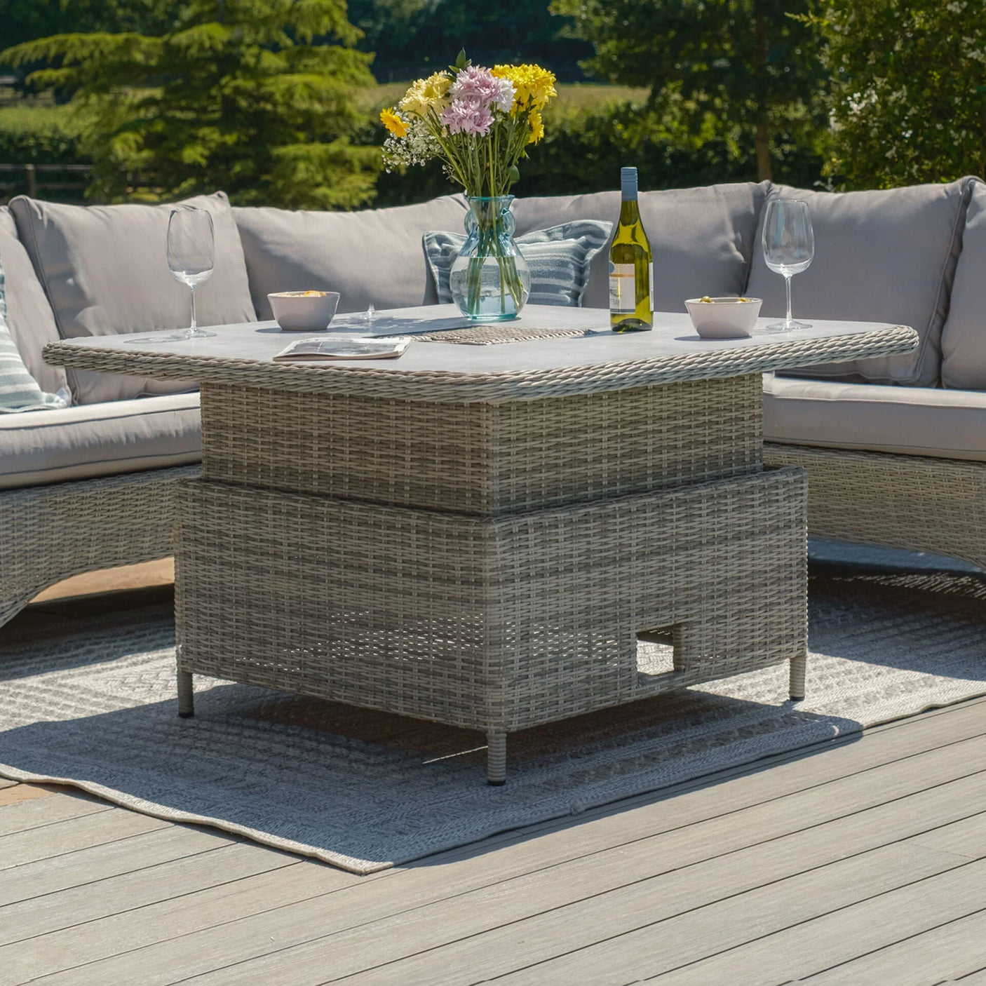 Grey rattan garden corner sofa with glass top table, wine, flowers, and outdoor rug