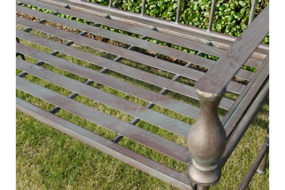 Metal garden bench seat slats and armrest detail with greenery in background