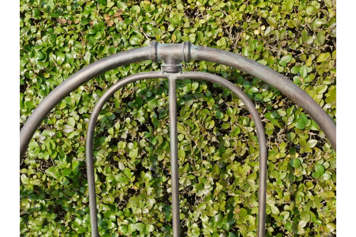 Black metal garden bench backrest close-up with curved design against green hedge