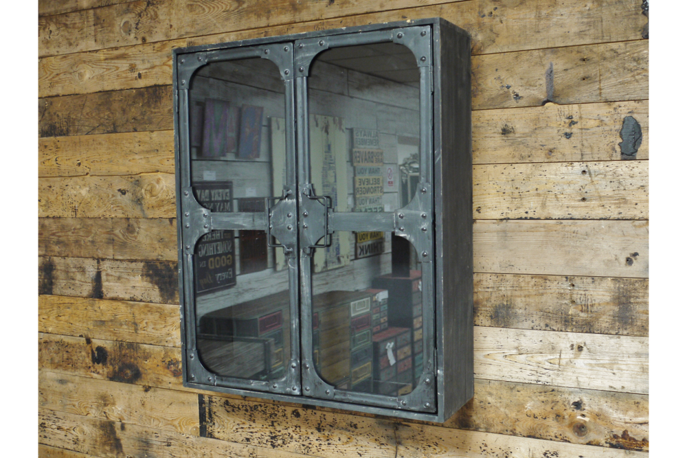 Metal wall cabinet with glass double doors, rivet details, mounted on rustic wooden plank wall, angled view.