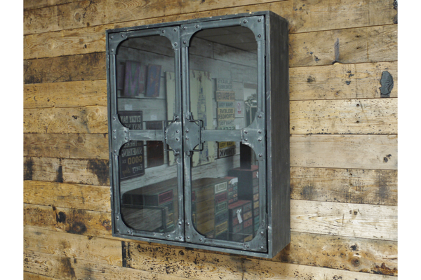 Metal wall cabinet with glass double doors, rivet details, mounted on rustic wooden plank wall, angled view.
