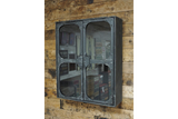Wall-mounted black metal wall cabinet with two glass doors, viewed from a slight side angle against a wooden plank wall.
